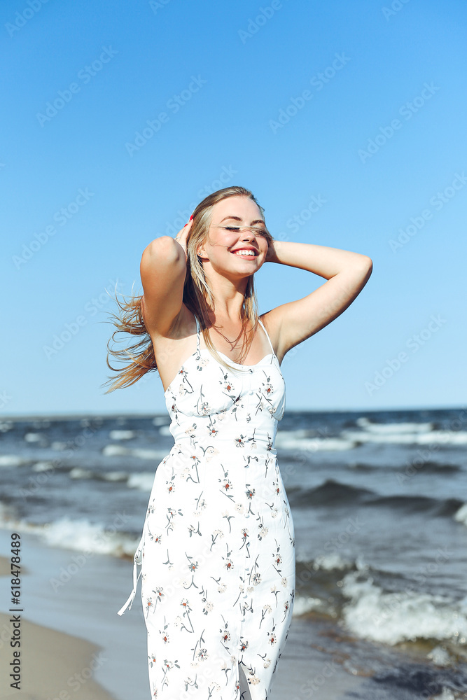 Happy blonde woman in free happiness bliss on ocean beach standing straight. Portrait of a female model in white summer dress enjoying nature during travel holidays vacation outdoors Happy blonde woman in free happiness bliss on ocean beach standing straight. Portrait of a female model in white summer dress enjoying nature during travel holidays vacation outdoors