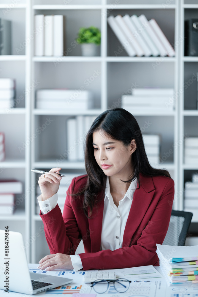 thinking Beautiful asian businesswoman working on laptop and calculating with financial calculator from statistics data graphs, charts. modern office wear red shirt. thinking Beautiful asian businesswoman working on laptop and calculating with financial calculator from statistics data graphs, charts. modern office wear red shirt.