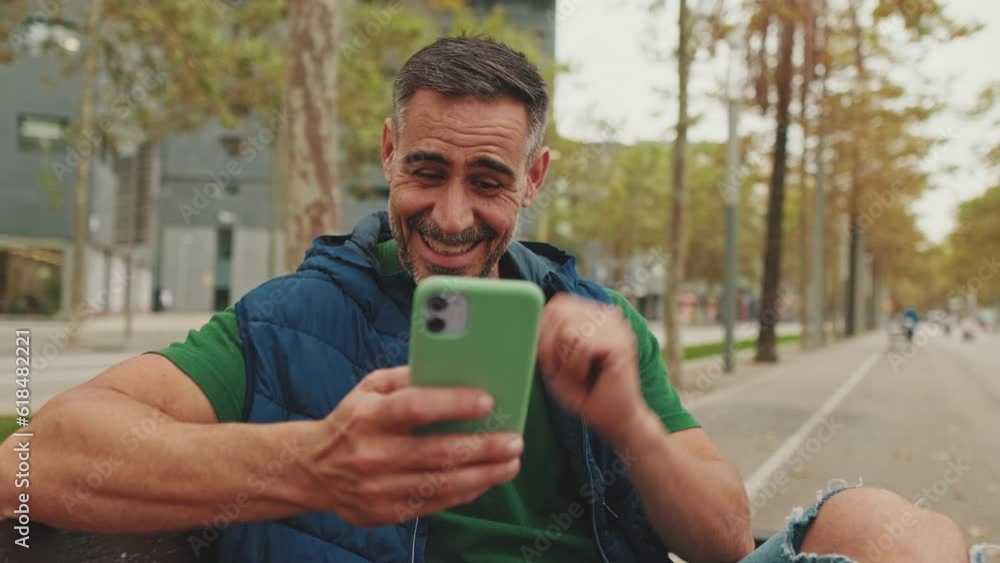 Middle-aged man sitting on bench talking on video call from mobile phone Middle-aged man sitting on bench talking on video call from mobile phone