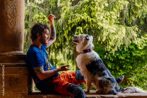 young white man sitting next to his border collie dog in an old building with a forest in the background. man training and playing with his pet