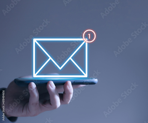 Businessman hand and glowing email icon on smartphone, email marketing concept The company sends bulk emails or digital newsletters to its customers.