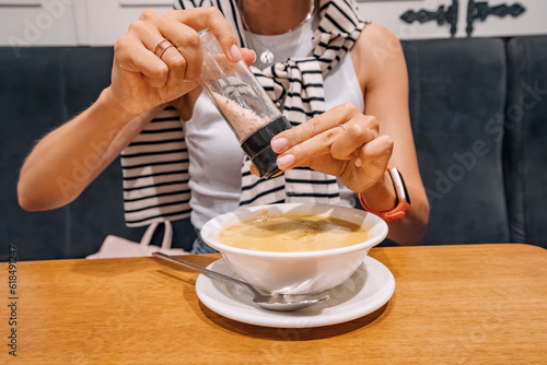 A woman adds salt from a saltcellar to soup in a restaurant. An overabundance of consumption of this seasoning can lead to cardiovascular diseases and gout