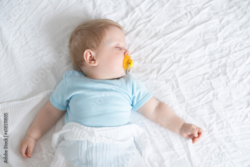 A baby with a pacifier in his mouth is sleeping on the bed photo