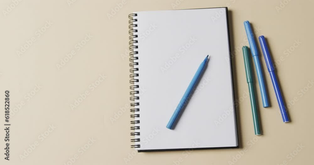 Overhead view of notebook with blue markers on beige background, in slow motion Overhead view of notebook with blue markers on beige background, in slow motion