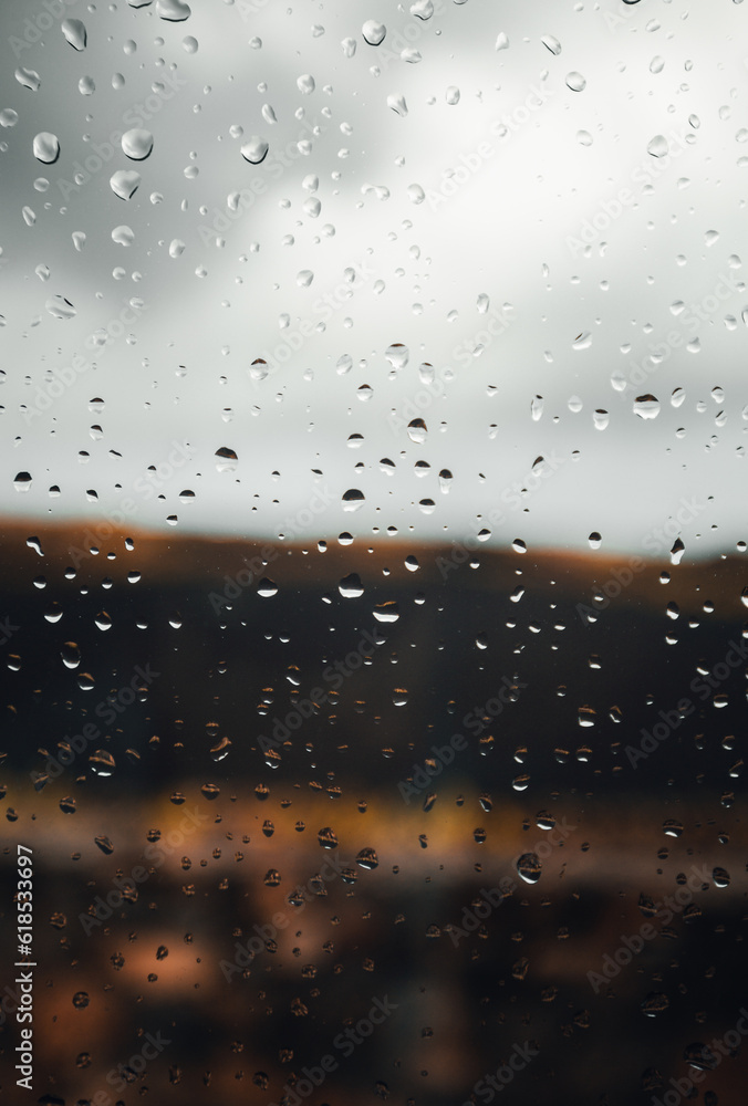 Close up image of raindrops on the window with cloudy sky on background. Vertical image of rain drops on the glass with outdoor on background in rainy day