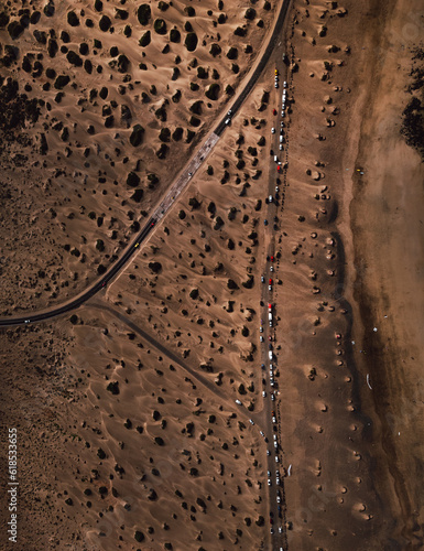 Aerial vieiw of road with parked cars on the side in dry sand dunes. Top view  - vertical photo of sand beach on the coast with vehicles on the road.