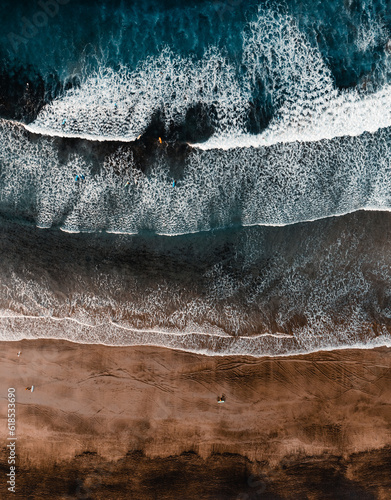Top view by drone of yellow sand beach with ocean and waves. Beach with surfers on the beach at sunny day from above - vertical photo.