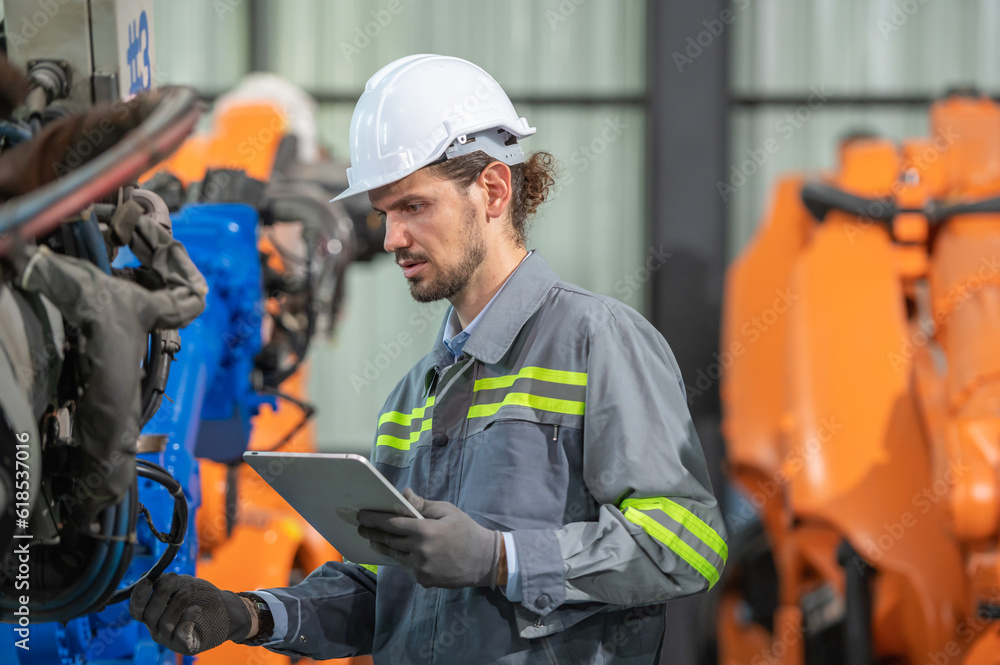 male automation engineer in uniform helmet safety inspection check control heavy machine robot arm system in industrial factory. technician worker check for repair factory machine male automation engineer in uniform helmet safety inspection check control heavy machine robot arm system in industrial factory. technician worker check for repair factory machine