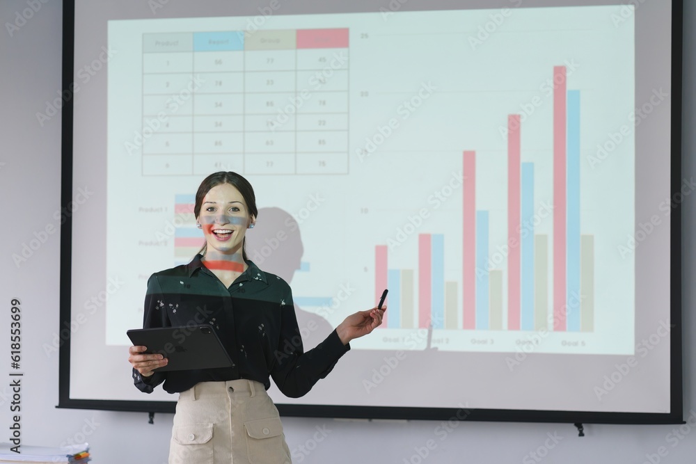 The female Chief Analyst is conducting a meeting presentation for a team of economists. The projector screen shows graphs, product sales, revenue growth strategies, and e-commerce analysis. The female Chief Analyst is conducting a meeting presentation for a team of economists. The projector screen shows graphs, product sales, revenue growth strategies, and e-commerce analysis.