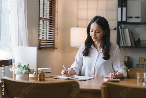 Young Asian female working with financial papers at home, using a calculator to count before paying taxes and receipts online. The millennial woman planning budget for saving money.