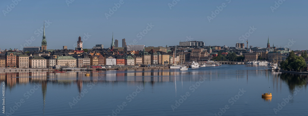 Panorama, view over the bay Strömmen, the old town Gamla Stan, boats marooned at piers, water reflecting, mirror reflections, a sunny summer morning in Stockholm