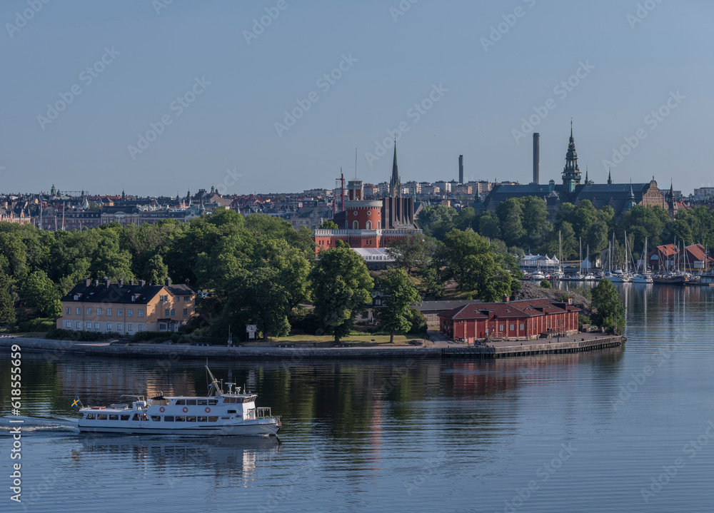 Archipelago ferry in the bay Strömmen passing the castle on the island Kastellholmen, mirror water reflecting, a sunny summer morning in Stockholm