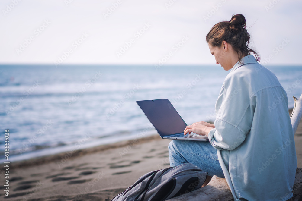 Young caucasian woman freelancer working on a laptop while sitting on a sandy beach.