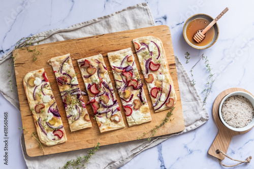 Baked tarte flambee with rhubarb, red onions, goat cheese and honey, cut into strips,  marble background photo