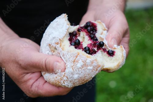 Donut or ponchik in male hands. Traditional donut with blueberries. Sugar powder. Local small food business. lake Svitiaz, Shatsk National Natural Park, Ukraine.