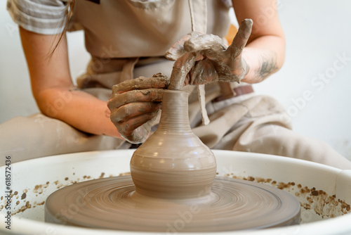close up of ceramist hands working and shaping ceramic vase on the lathe or potter's wheel inside a pottery workshop with natural light