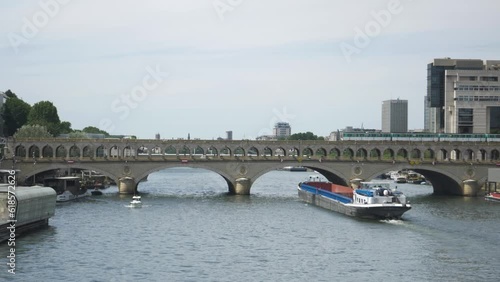 A barge sails on the river while a subway passes over the bridge