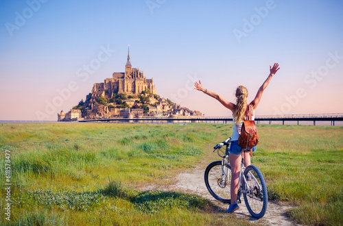 Happy woman tourist in bicycle enjoying view of Le Mont Saint Michel at sunrise- Normandy in France