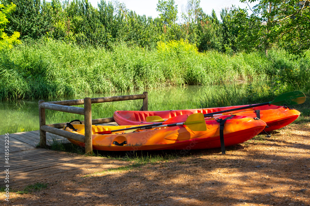 Canoas roja y naranja a la sombra en la orilla de un río.