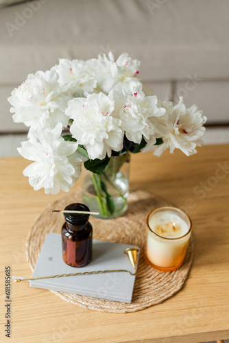 Home cozy interior. Candles, a bouquet of peonies in a glass vase on a wooden coffee table. Spring.