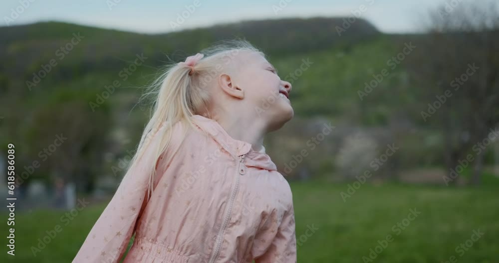 Fair-skinned blonde child girl in pink jacket on outside on green meadow while flower petals or snow are flying. Fair-skinned blonde child girl in pink jacket on outside on green meadow while flower petals or snow are flying.