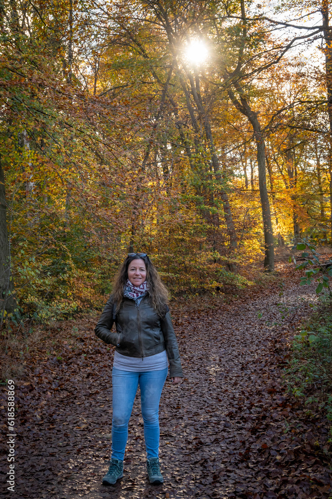 Lady hiking in autumn woodland setting with yellow and brown leaves on the floor and sun breaking through the trees. Single Dutch woman on countryside walk in fall. Lage Vuursche in the Netherlands Lady hiking in autumn woodland setting with yellow and brown leaves on the floor and sun breaking through the trees. Single Dutch woman on countryside walk in fall. Lage Vuursche in the Netherlands