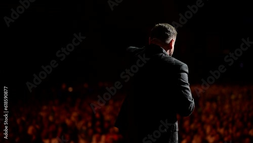 Presentation at a business conference for office workers. The speaker addresses the audience on stage in a crowded hall. An adult man explains motivation to a group of people.