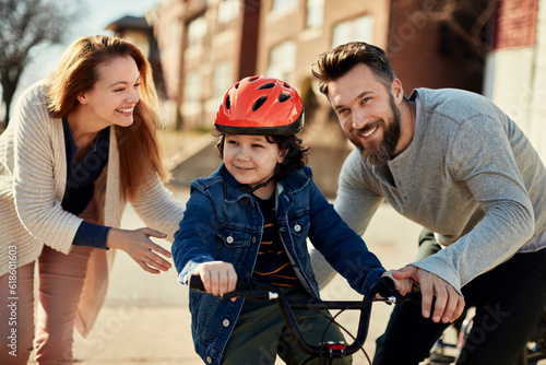 Young boy riding a bike with his parents next to him on a sidewalk in the suburbs