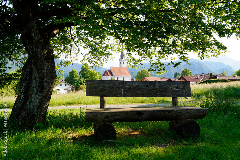a serene and peaceful alpine scenery with a rustic wooden bench on a sunny summer day in the Bavarian village Schwangau in the Bavarian Alps, Bavaria, Germany	