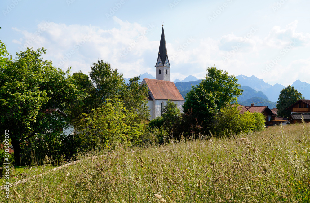 a scenic alpine view with lush green alpine meadows and an old church in the alpine village Schwangau in the Bavarian Alps on a summer day (Allgaeu, Bavaria, Germany)  