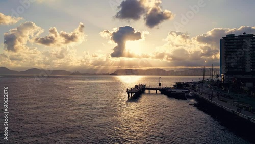 Drone video approaching a fishing deck in a beautiful sunset reflected in the sea. Pier with people fishing and looking out to sea. Santos, Brazil.