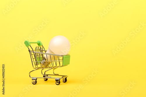 A small lightbulb in a toy supermarket cart on a yellow background. High quality photo