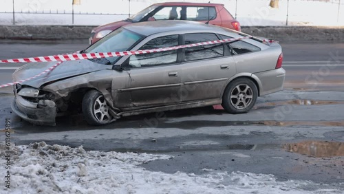 Barrier tape, accident on street, car accident. Vehicle, front-end heavily damaged after crash, enclosed by emergency tape.