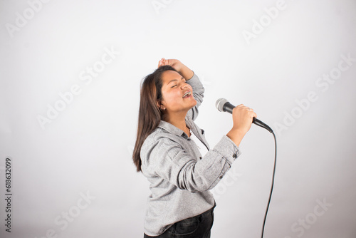 photo of latin woman singing passionately with a microphone on light studio background. Concept of people and hobbies.