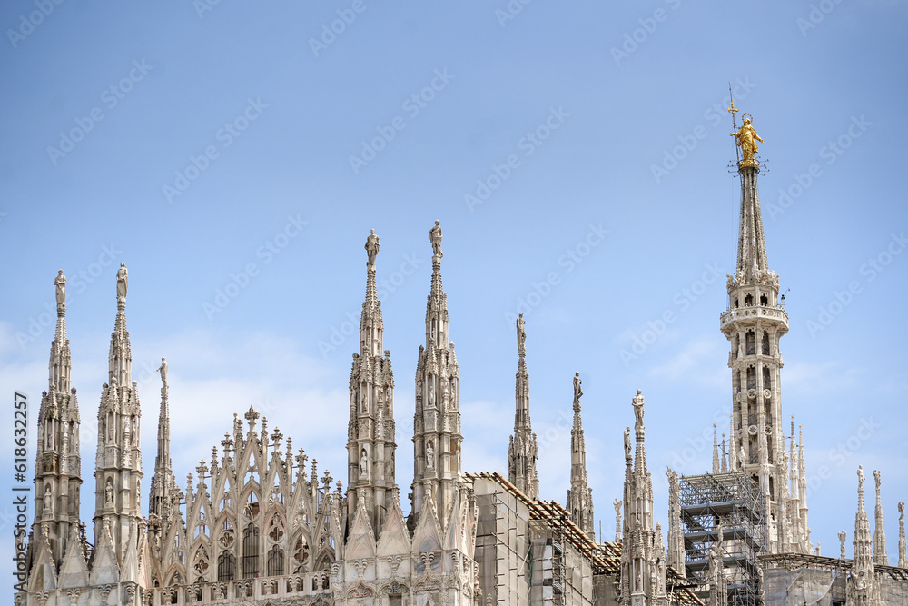 Milan Cathedral roof, Italy. Famous  Duomo di Milano is a top landmark of Milan. Many luxury spires with statues on blue sky background. Beautiful Gothic architecture of Milan city