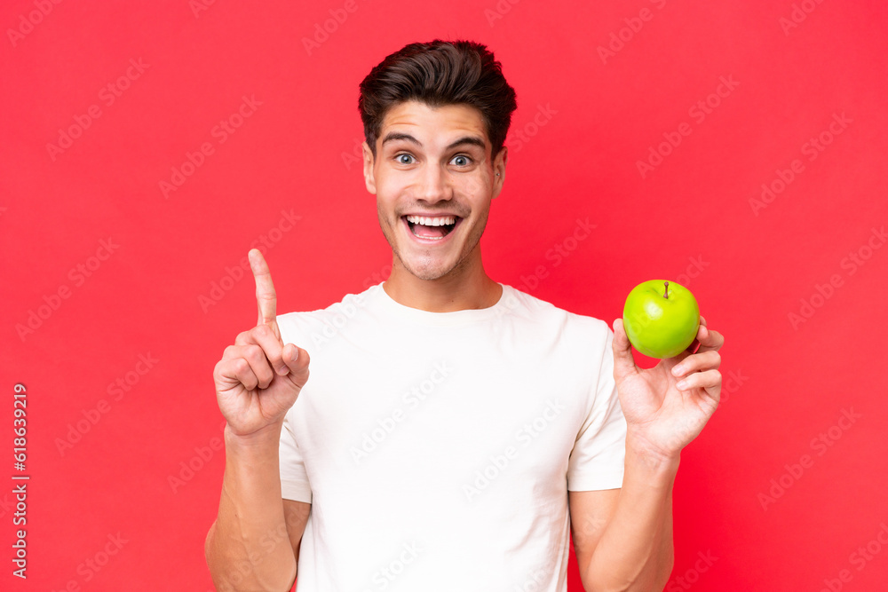 Young caucasian man with an apple isolated on red background pointing up a great idea Young caucasian man with an apple isolated on red background pointing up a great idea