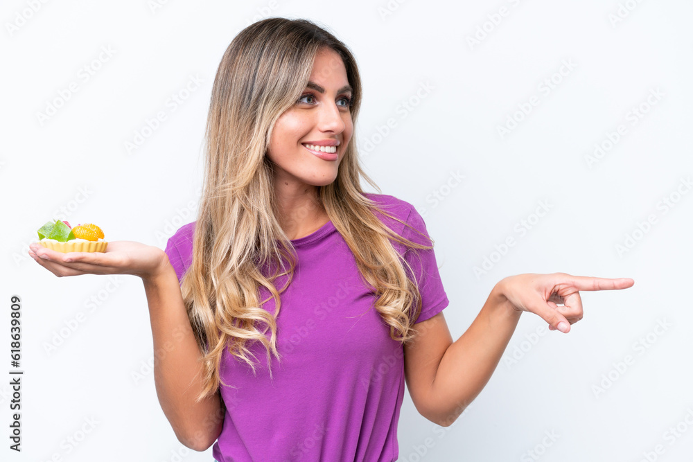Young pretty Uruguayan woman holding a tartlet isolated on white background pointing to the side to present a product Young pretty Uruguayan woman holding a tartlet isolated on white background pointing to the side to present a product