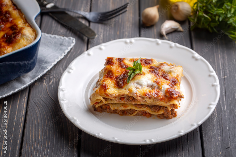 Portion of ground beef lasagna topped with melted cheese and garnished with fresh parsley served on a plate in close view for a menu Portion of ground beef lasagna topped with melted cheese and garnished with fresh parsley served on a plate in close view for a menu
