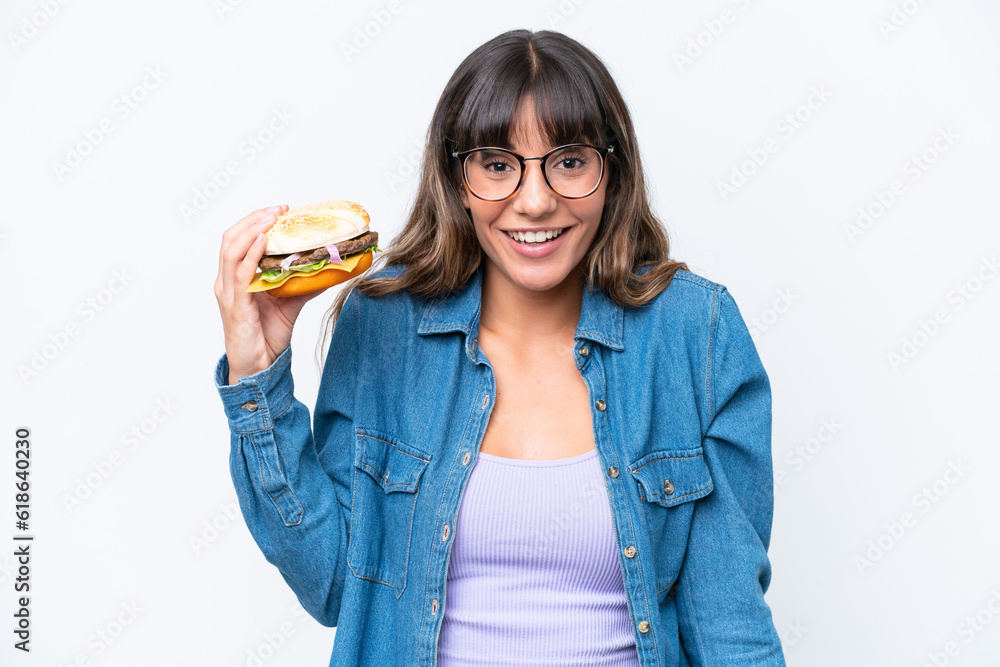 Young caucasian woman holding a burger isolated on white background with surprise and shocked facial expression Young caucasian woman holding a burger isolated on white background with surprise and shocked facial expression
