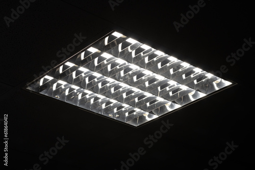 Fluorescent lamps in square lampshade in dark room.