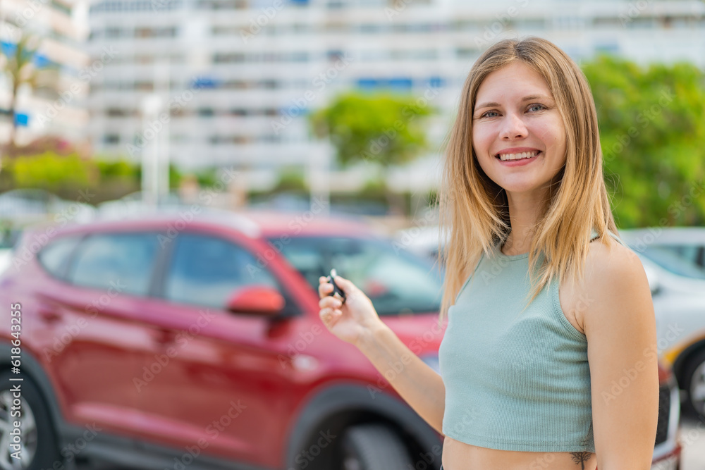 Young blonde woman at outdoors holding car keys with happy expression
