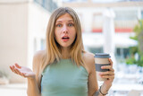 Young blonde woman holding a take away coffee at outdoors with shocked facial expression