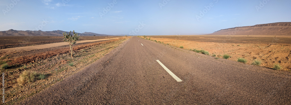 Panorama of an empty long straight road in south Morocco, surrounded by an arid landscape