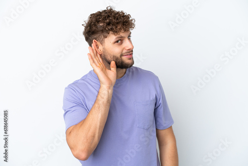 Young handsome caucasian man isolated on white background listening to something by putting hand on the ear
