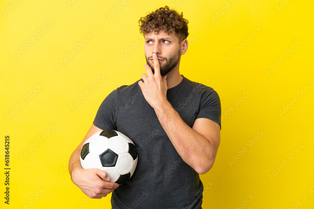 Handsome young football player man isolated on yellow background having doubts while looking up Handsome young football player man isolated on yellow background having doubts while looking up