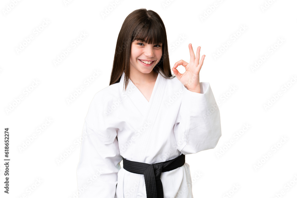 Little Caucasian girl doing karate over isolated background showing ok sign with fingers Little Caucasian girl doing karate over isolated background showing ok sign with fingers