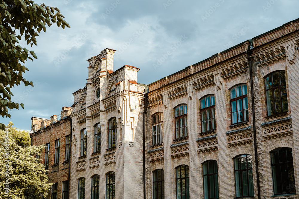 Facade of an old brick building with a tower. Building against the sky. Beautiful old architecture. University park. Tourist place of Kyiv. Gothic architecture.