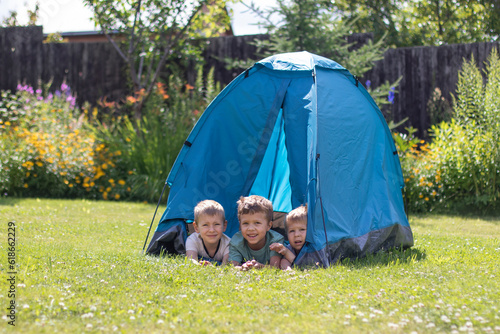 Three little boys lie in a blue tourist tent in the yard. 