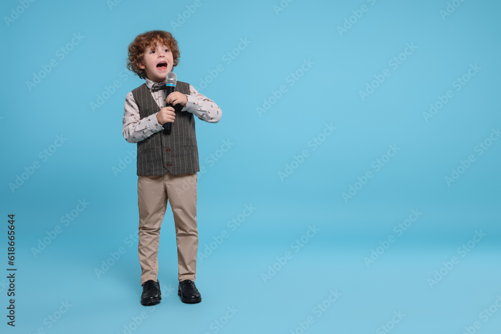 Cute little boy with microphone singing on light blue background, space for text Cute little boy with microphone singing on light blue background, space for text