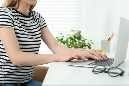 Home workplace. Woman typing on laptop at white desk indoors  closeup